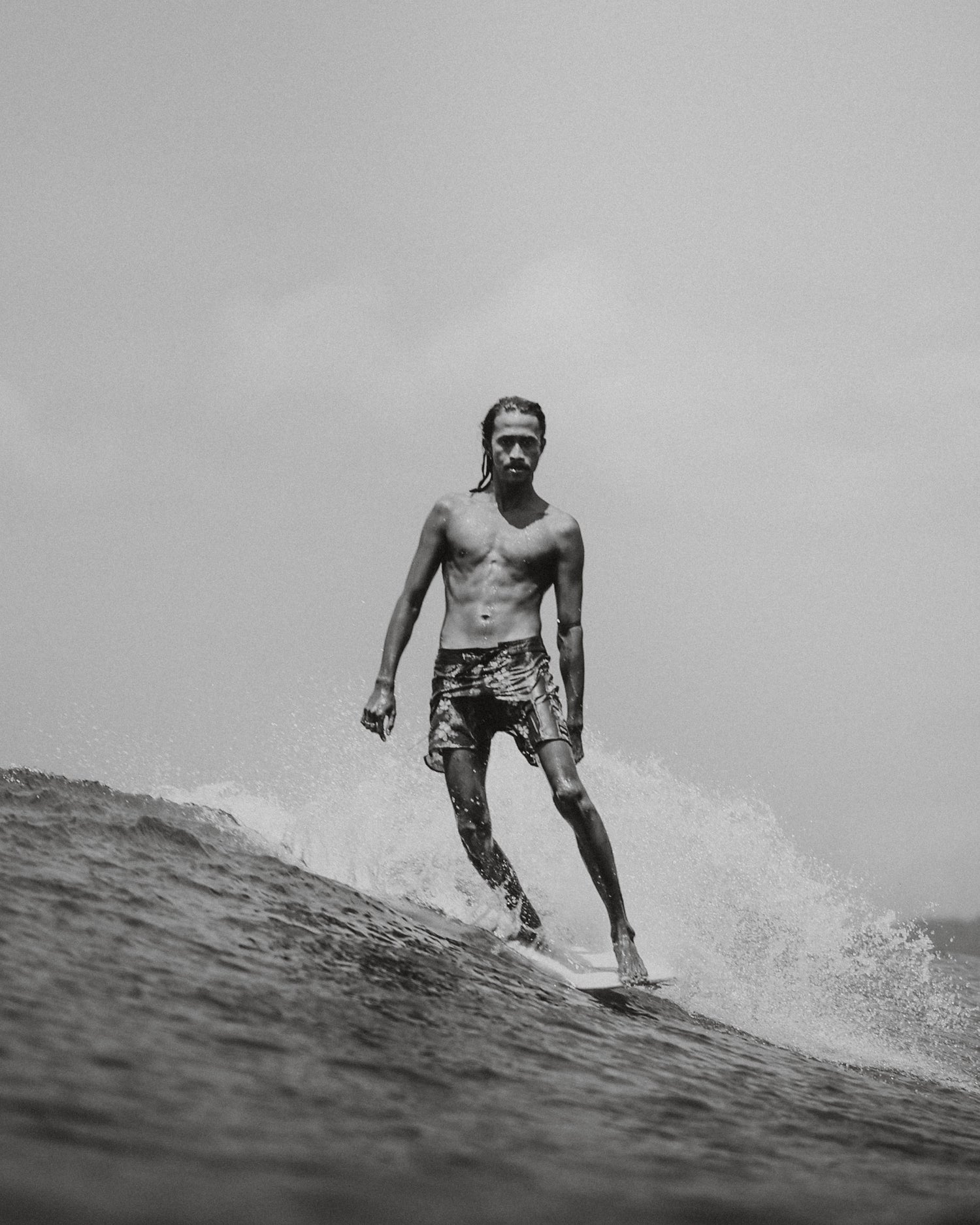 Black and white lifestyle image of a local Indonesian surfer longboarding at Inside Gerupuk on Lombok on a sunny warm day.